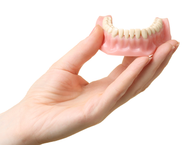 Hand holding a bottom plate of dentures which is a common and cost effective restorative dentistry service to restore a smile.